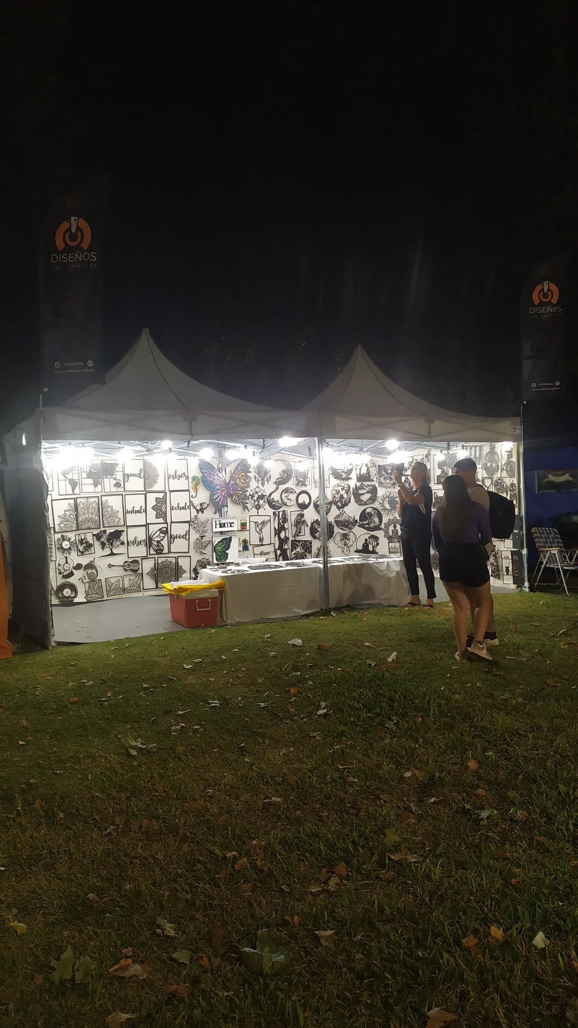 Stand de CC Design iluminado de noche con banners y cuadros decorativos en MDF